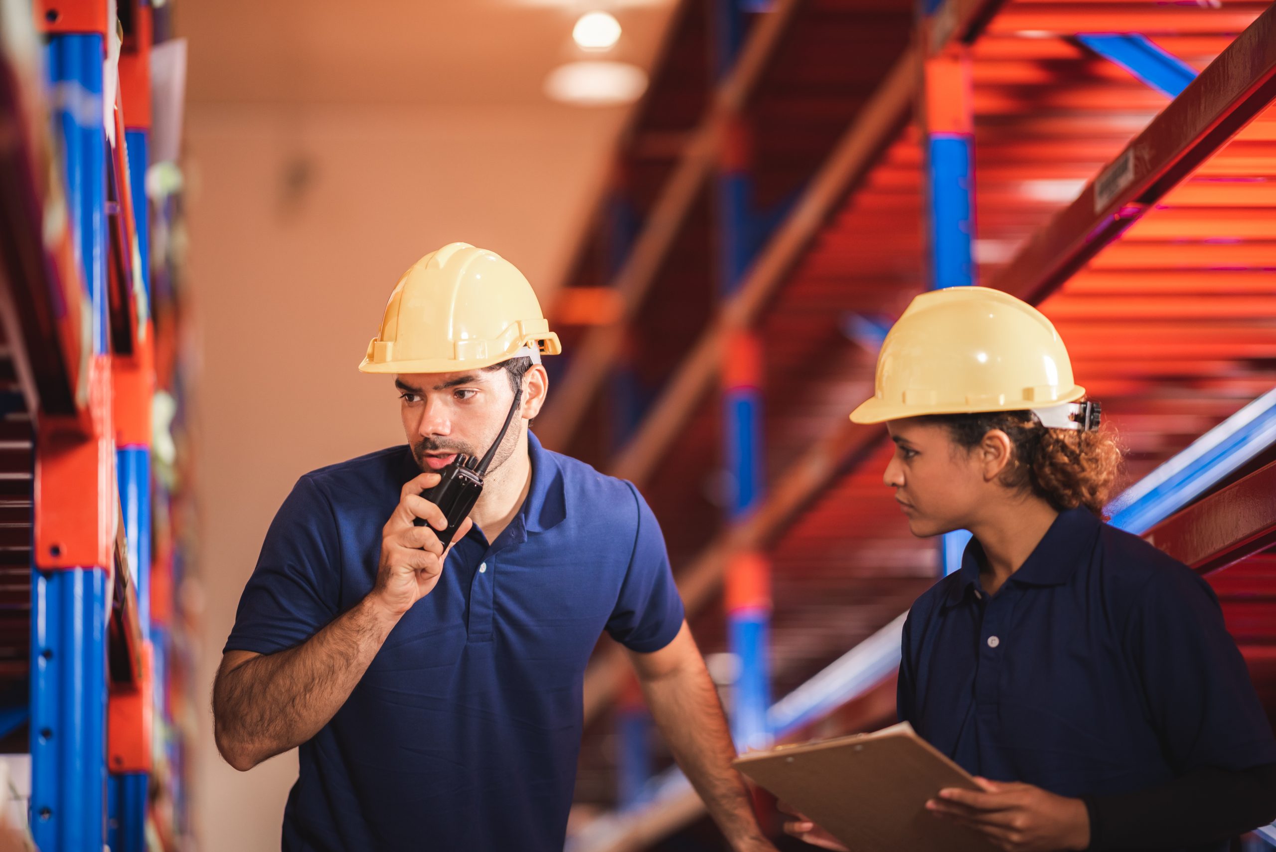 Male dispatcher, warehouse worker checking packages while using walkie-talkie in distribution warehouse storage.