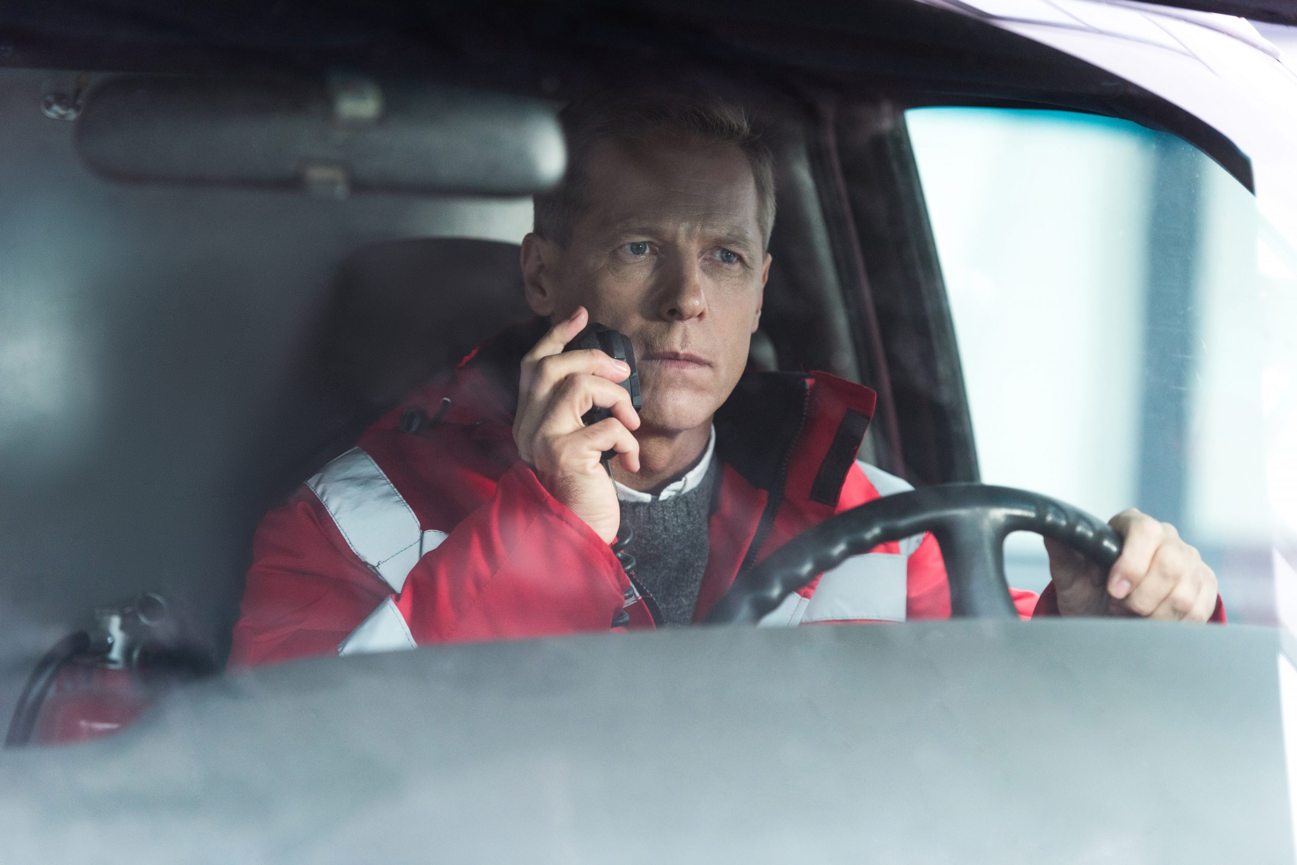 serious paramedic sitting in ambulance on driver seat and talking by portable radio